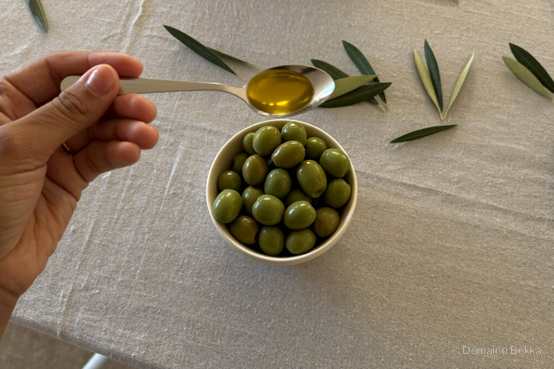 Cuillerée d’huile d’olive au-dessus d’un bol d’olives vertes