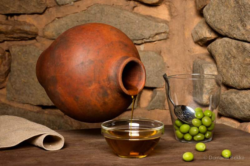 Huile d’olive versée d’une cruche en terre dans un bol de verre