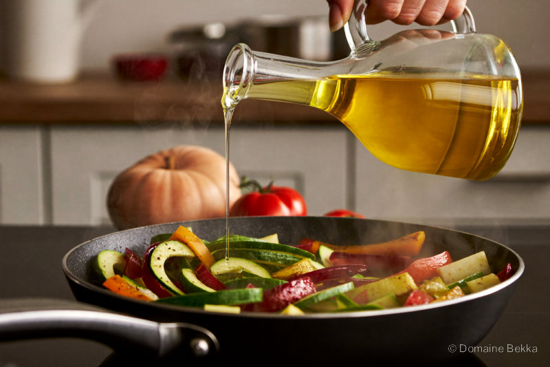 Huile d’olive versée sur une poêlée de légumes d’été