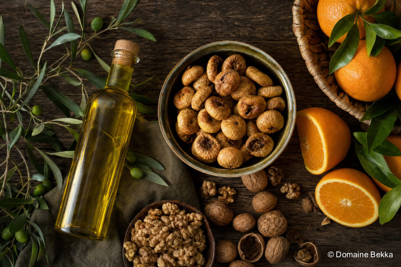Assortiment de produits du terroir algérien : huile d’olive, figues sèches, agrumes et noix sur une table rustique