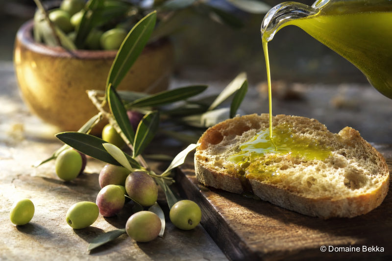Huile d’olive nouvelle verte versée sur du pain, olives fraîches